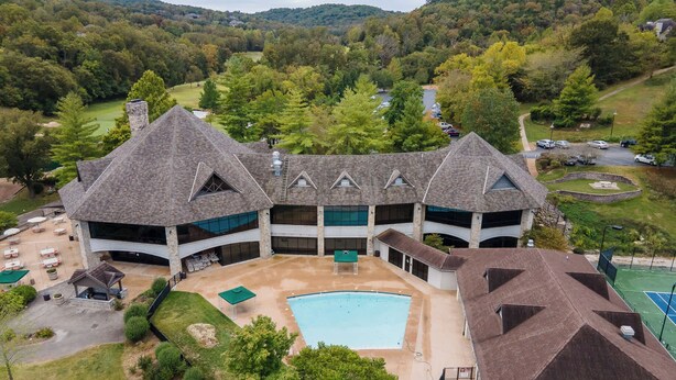 A large, multi-story building with a central courtyard, a swimming pool, and a tennis court. - Birdie Lane Beauty – Golf, Pools, Gym, & More! (Branson West)
