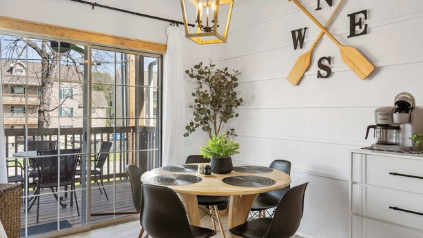 A modern dining area with a round wooden table, black chairs, a potted plant, and a wall-mounted sign with wooden paddles spelling "WES". - Our Landing Place | Access to Pool! (Branson)