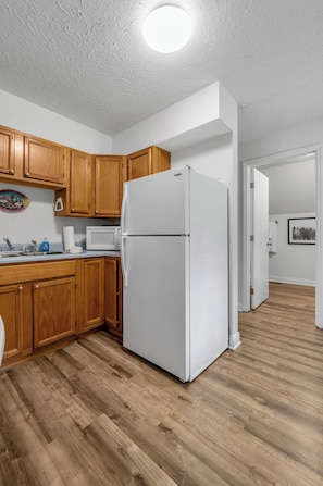 Une cuisine avec des meubles de rangement en bois, un réfrigérateur blanc et un plancher en bois.