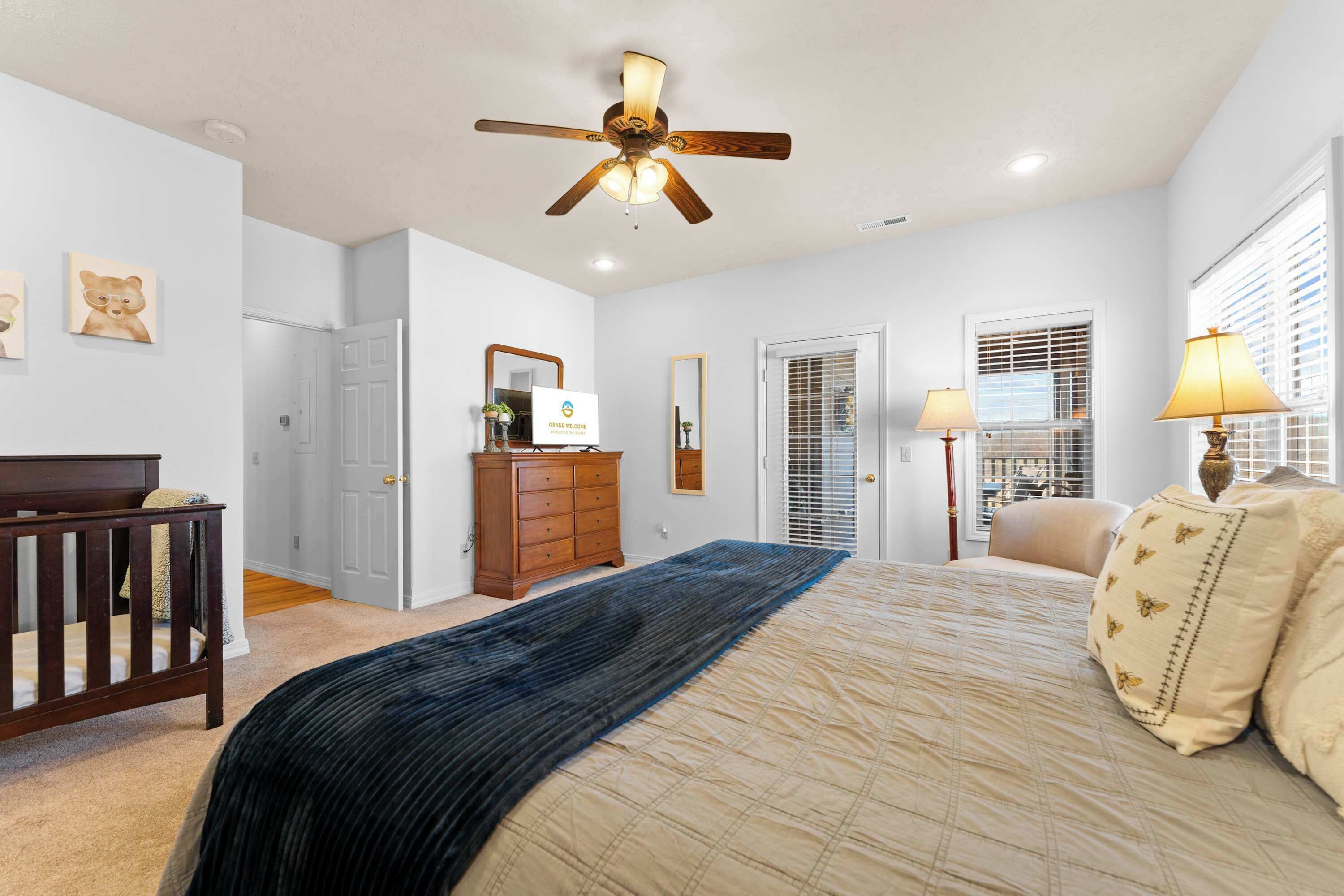A bedroom with a bed, a ceiling fan, a dresser, a nightstand, a lamp, and a window with blinds.