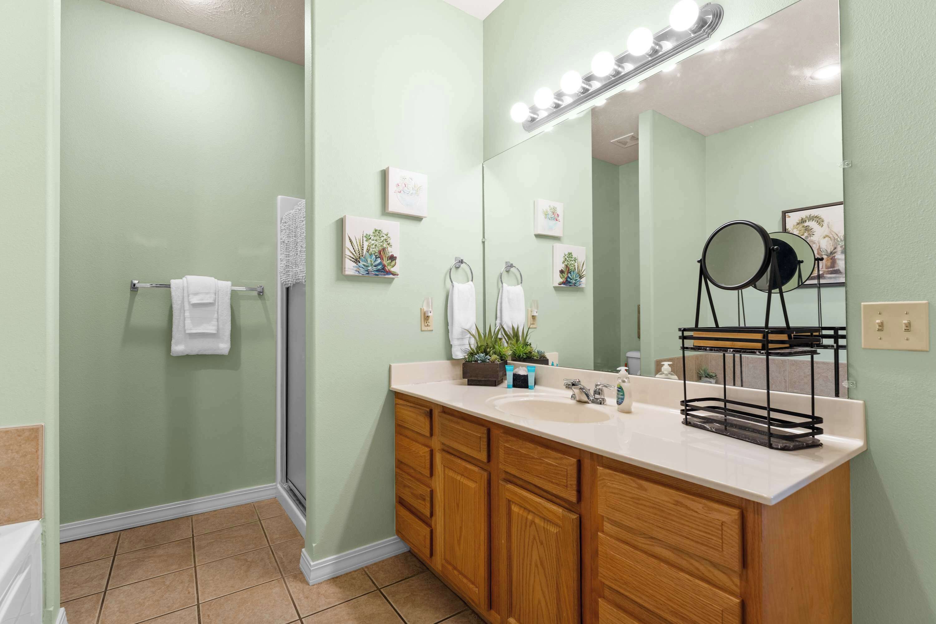 A bathroom with a green wall, wooden cabinets, a white sink, and a mirror with lights.