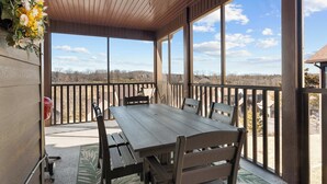 A covered patio with a wooden table and chairs, large windows, and a view of the landscape. - Honey Bee Inn w/ Communal Amenities & More! (Branson West)