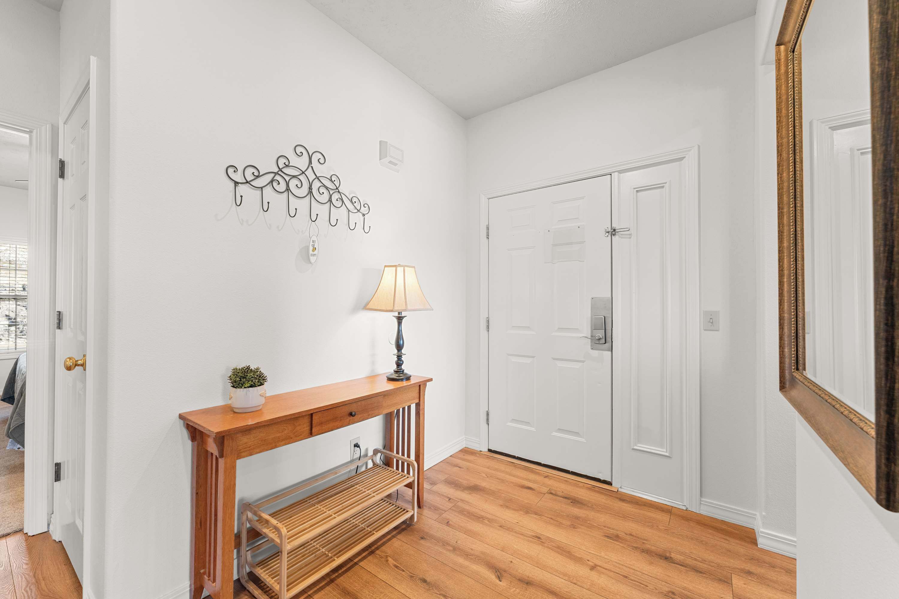 A hallway with a wooden console table, a lamp, a small plant, and a radiator. There are white doors and a white wall with a decorative metal piece.