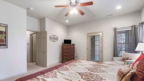 A bedroom with a bed, a dresser, a ceiling fan, a television, and a window with curtains.