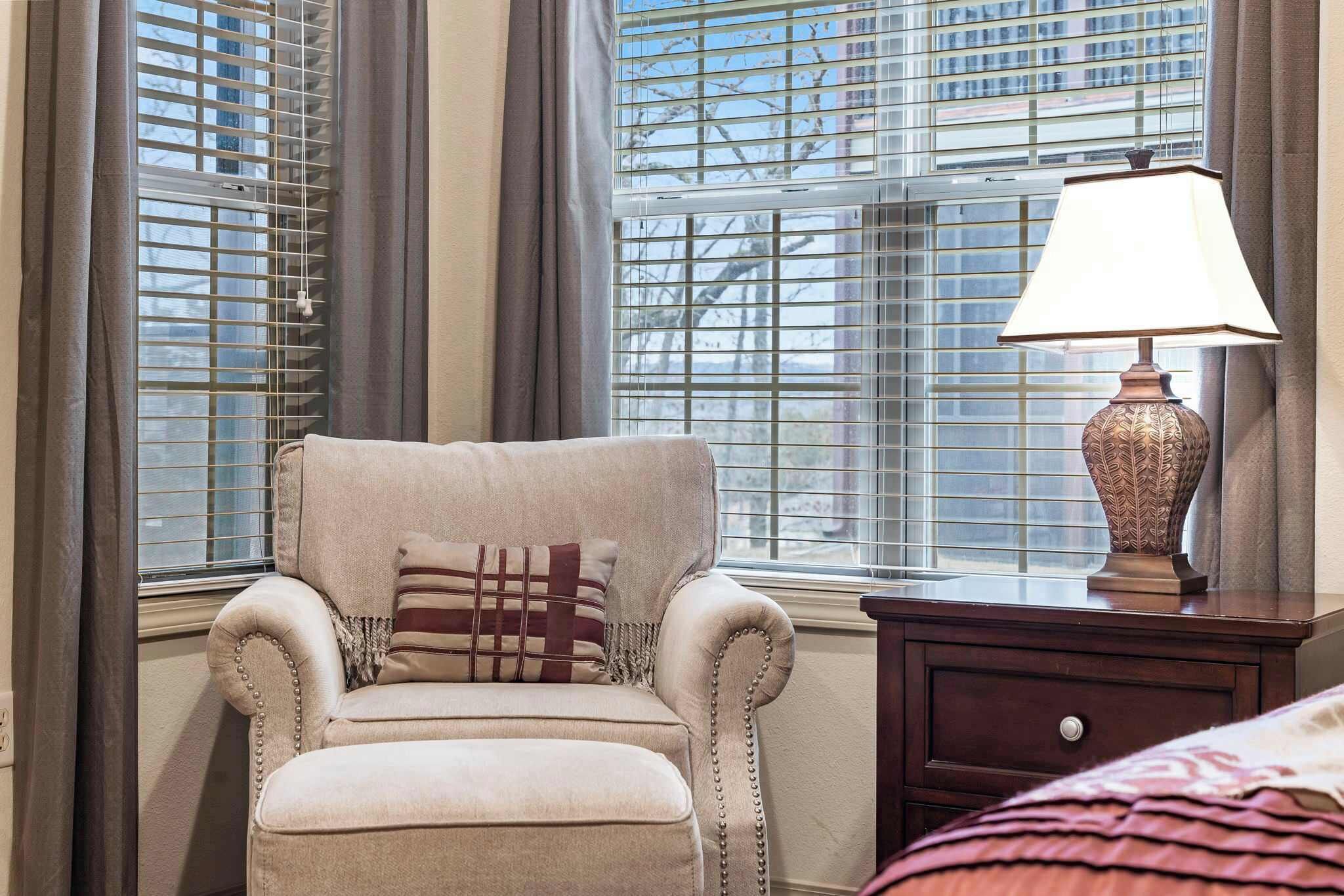 Una habitación con un sillón color beige, una lámpara y una ventana con persianas.
