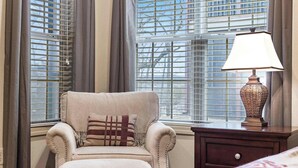 A room with a beige armchair, a lamp, and a window with blinds.