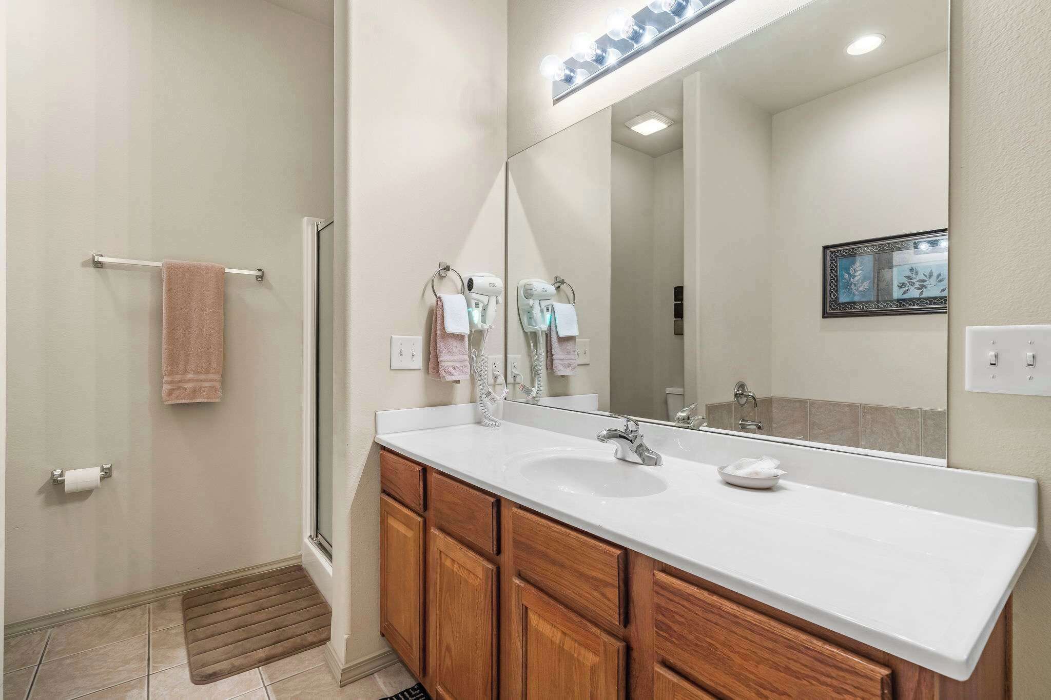 A modern bathroom with a large mirror, a white sink, wooden cabinets, and a glass shower enclosure.