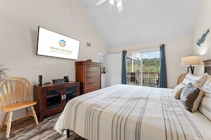 A bedroom with a bed, a dresser, a chair, a desk, a TV, and a balcony with a view.