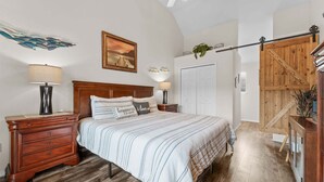 A bedroom with a wooden bed, two bedside tables, a nightstand, a wall-mounted lamp, a framed picture, a closet, and a wooden staircase. - On Lake Time Taneycomo - Amazing Views (Branson)