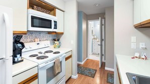 Una cocina con estufa, microondas y armarios. Hay una alfombra en el suelo y una puerta que da a otra habitación.