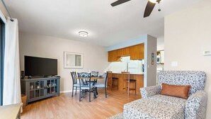 Una sala de estar con sofá, televisor, mesa de comedor, sillas y una cocina al fondo.