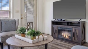 Un salon avec un canapé gris, une table basse ronde ornée de plantes en pot, une cheminée et un téléviseur fixé au mur.