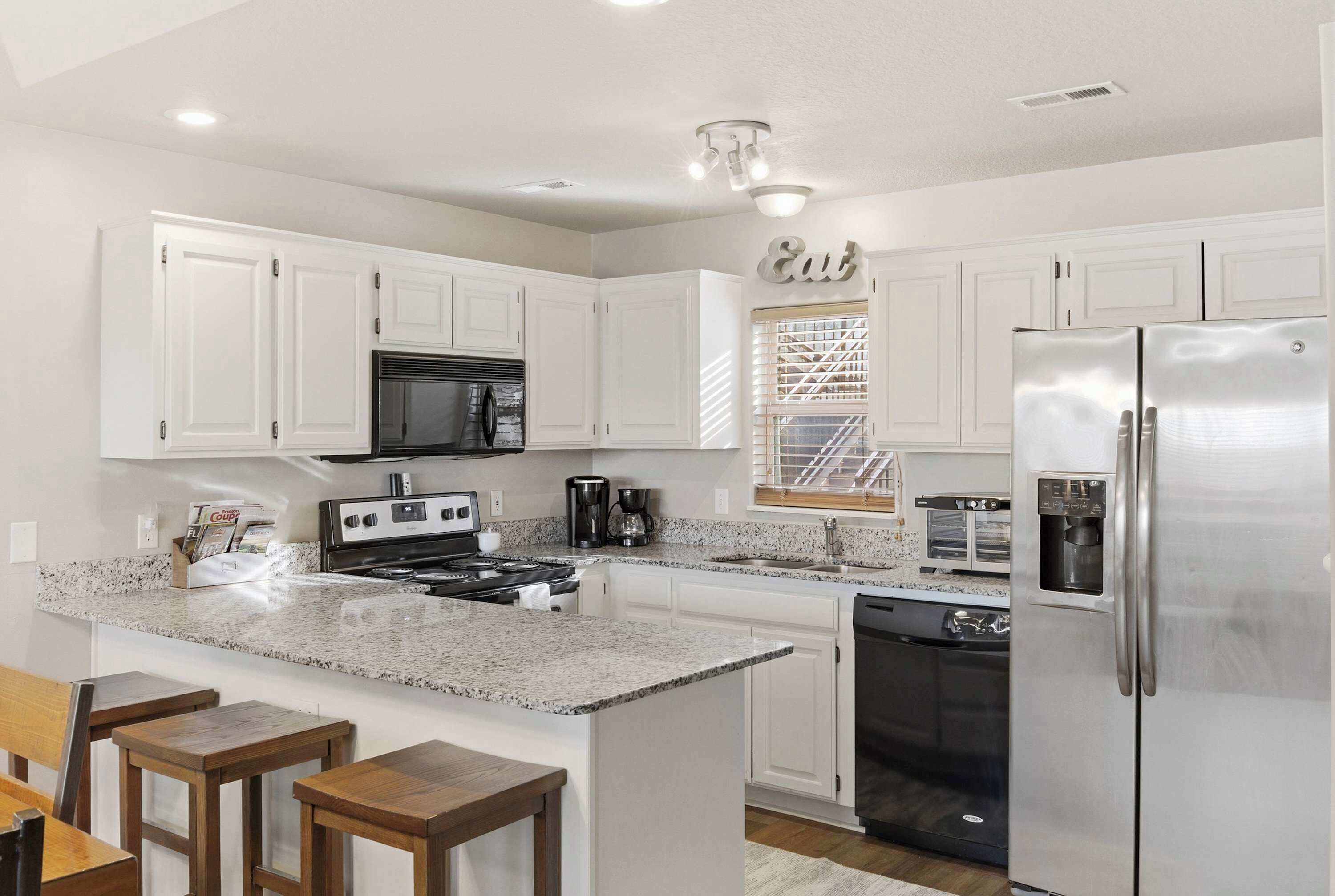 A modern kitchen with white cabinets, granite countertops, a stainless steel refrigerator, and a built-in oven.