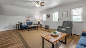 A living room with a ceiling fan, a blue sofa, a grey armchair, a wooden coffee table, and a rug.