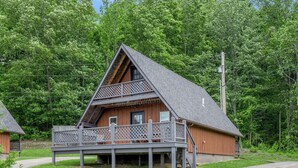 A wooden cabin with a balcony, surrounded by trees.