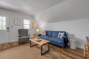 A living room with a blue sofa, a grey armchair, a wooden coffee table, and a small side table with a lamp.