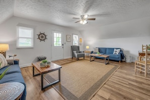 A spacious living room with a ceiling fan, a blue sofa, a gray armchair, and a wooden coffee table.