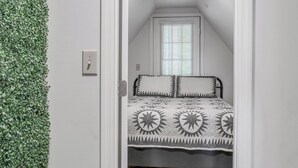 A narrow, sloped ceiling room with a bed, a window, and a wall-mounted switch.