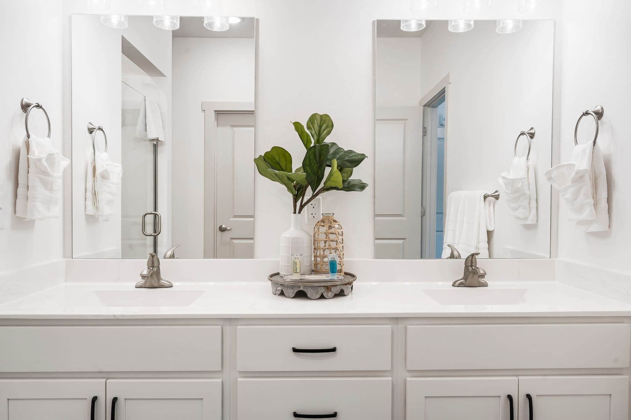 A modern bathroom with two sinks, a large mirror, and white cabinets.