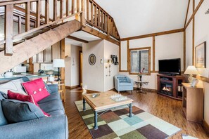 A cozy living room with a wooden staircase, a television, a fireplace, and a chessboard on a coffee table.