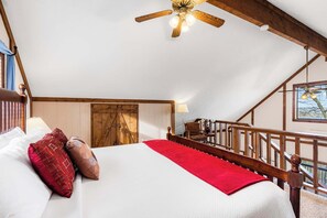 A bedroom with a wooden bed, a red throw blanket, a wooden ceiling fan, and a view of the outdoors.