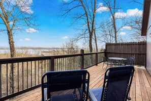 A wooden deck with two chairs and a table, overlooking a snowy landscape and trees.