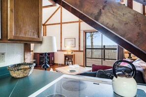 A cozy kitchen with a wooden ceiling, a dining table with a kettle, and a view of the outdoors.