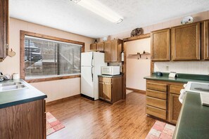A compact kitchen with wooden cabinets, a refrigerator, a microwave, and a sink. - Skipjack Cottage Branson (Branson West)