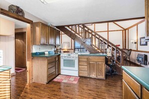 A kitchen with wooden cabinets, a stove, and a staircase. - Skipjack Cottage Branson (Branson West)