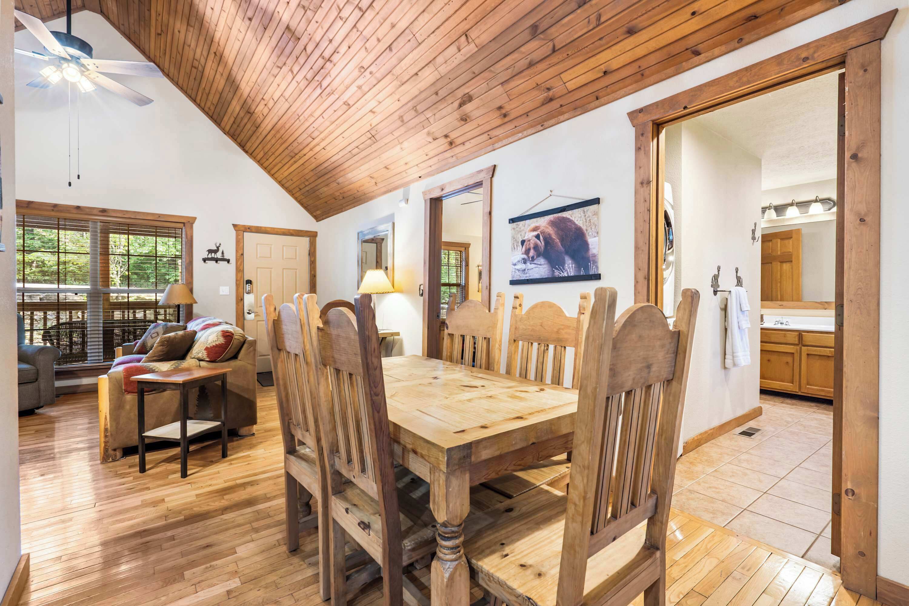 A dining area with a wooden table and chairs, a ceiling fan, and a view of the outdoors through large windows.