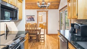 Una cocina con armarios de madera, un horno de acero inoxidable, una cafetera y un comedor con sillas y una mesa de madera.
