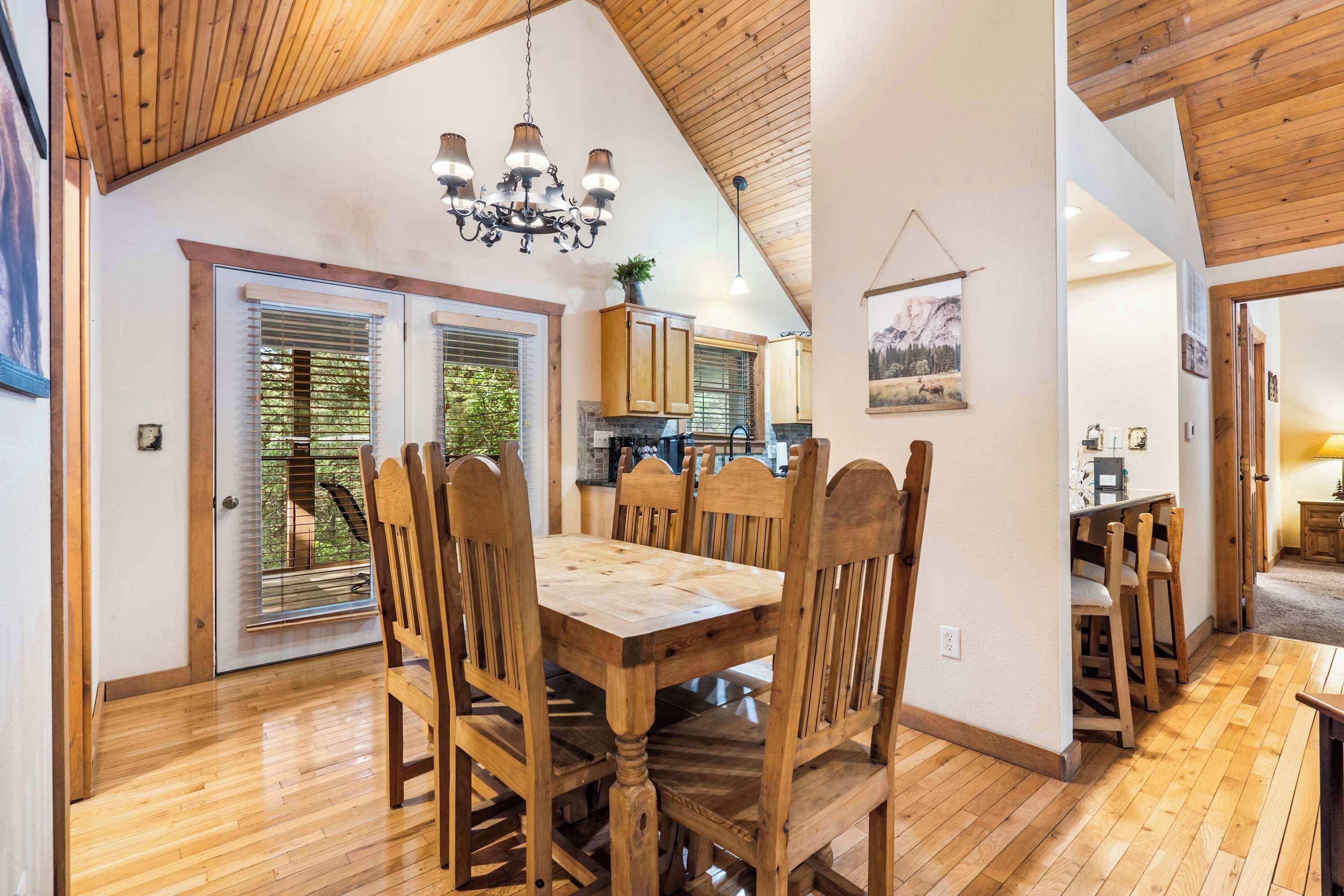 Un coin repas avec une table et des chaises en bois, un lustre et une vue sur la cuisine.