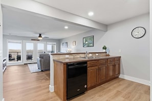 A modern kitchen with a dishwasher, wooden cabinets, and a large window overlooking a balcony. - Cozy Condo at Rock Lane Resort (Branson)