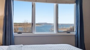 Ett sovrum med ett stort fönster som ger utsikt över en sjö och avlägsna kullar.