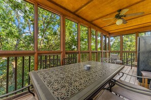A covered outdoor area with a table and chairs, a ceiling fan, and a view of trees. - Kemper's Cabin in the Ozarks | Onsite amenities (Branson)