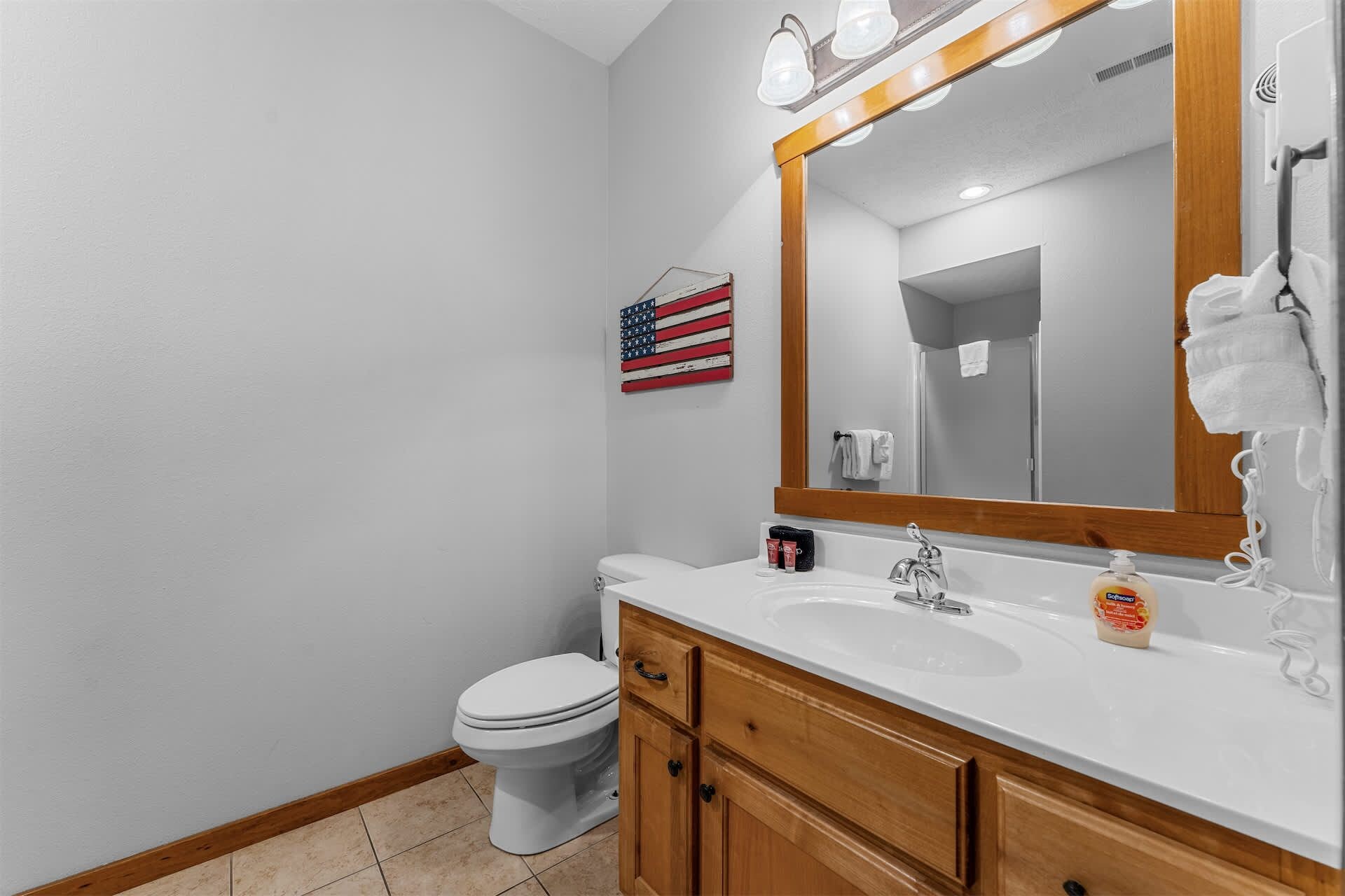 A bathroom with a white toilet, wooden vanity, and a large mirror.