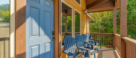 Un porche de madera con sillas Adirondack y una puerta azul.