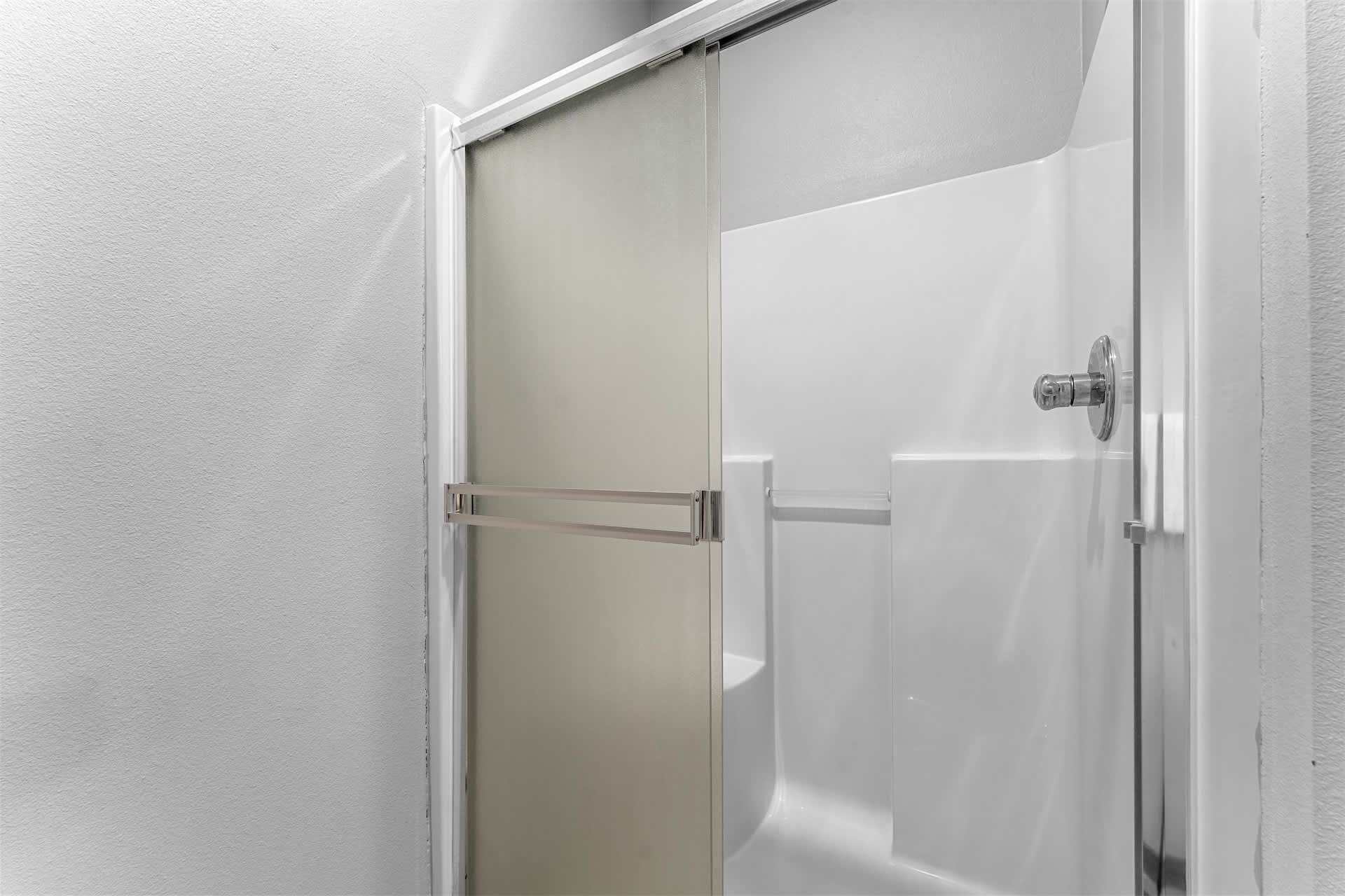 Une cabine de douche dotée d’une porte coulissante, d’un pommeau de douche et d’un porte-serviettes fixé au mur.