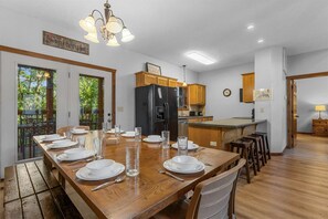 A dining area with a wooden table set for four, a black refrigerator, wooden cabinets, and a view of greenery through the door. - Kemper's Cabin in the Ozarks | Onsite amenities (Branson)