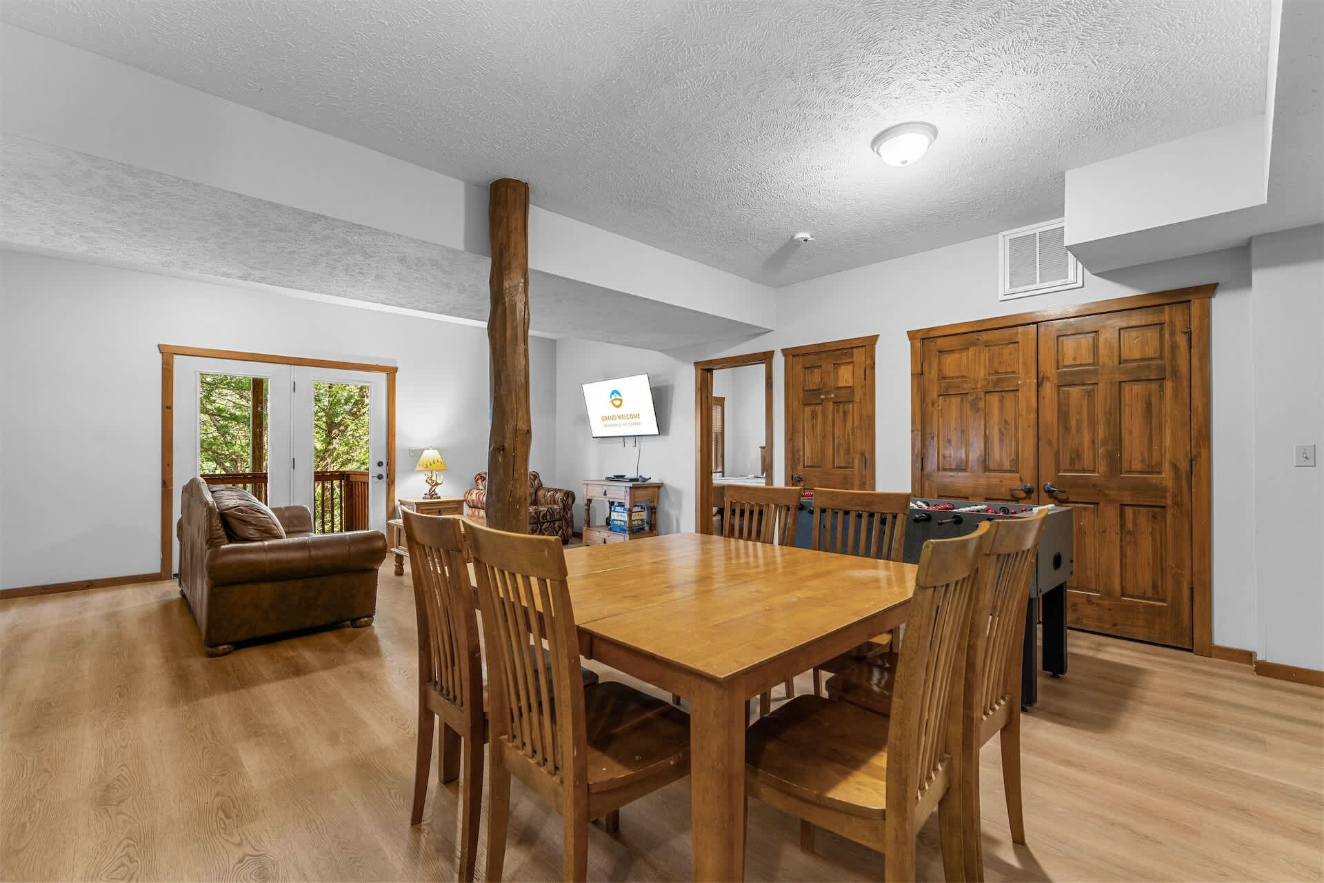 Un coin repas avec une table et des chaises en bois, un téléviseur fixé au mur et une grande porte en bois.