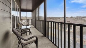 A covered balcony with wicker furniture and a view of a parking lot and buildings. - Rest Nest in the Heart of Ozark's Nature! (Branson West)
