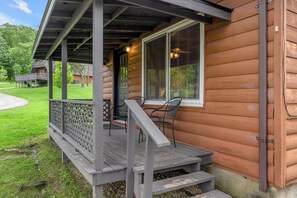 A wooden cabin with a porch, a covered deck, and a window with blinds.