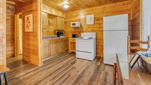 Interior de una cabaña de madera con cocina, que incluye armarios de madera, un microondas, una estufa y un refrigerador.