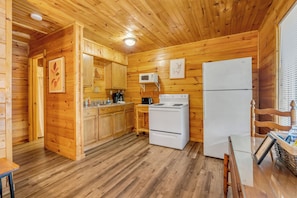 A wooden cabin interior with a kitchen area, including wooden cabinets, a microwave, a stove, and a refrigerator.