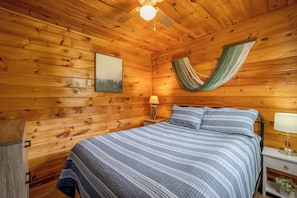 Una camera in una baita di legno, con un letto, un'amaca, un comodino con una lampada e un quadro appeso al muro.