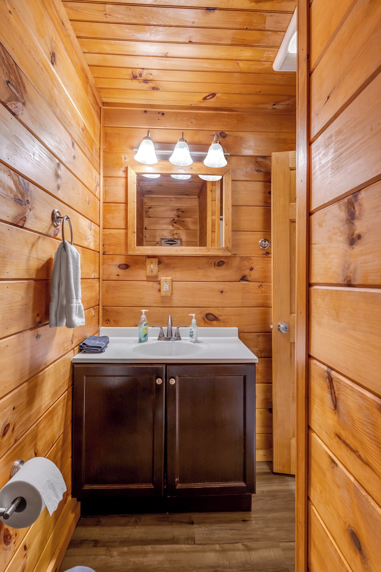 Baño de cabaña de madera con lavamanos, espejo y toallero.