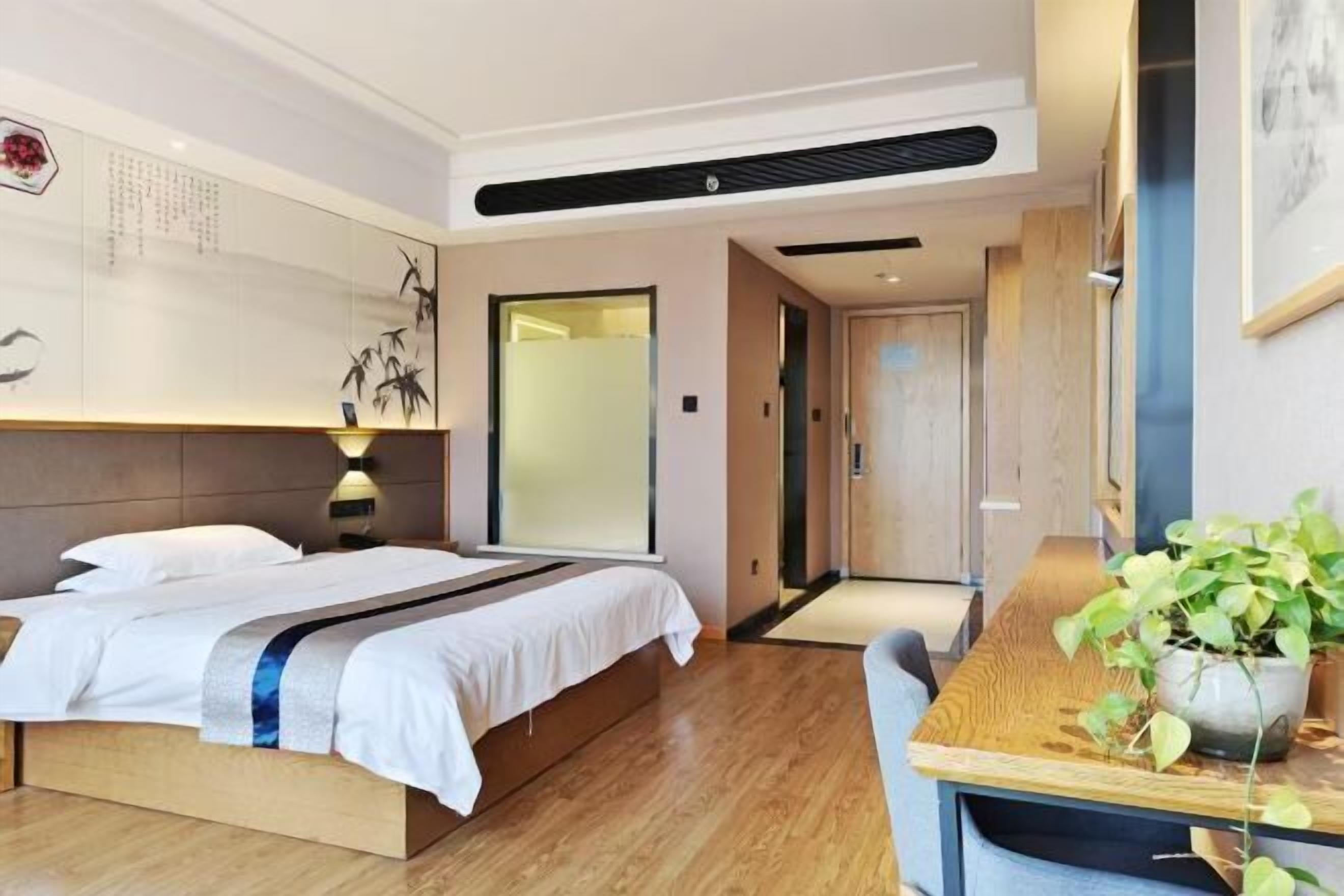 Une chambre d’hôtel moderne avec un lit en bois, un bureau agrémenté d’une plante et un mur décoré d’œuvres d’art.