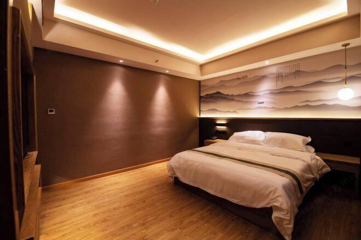 A modern bedroom with a wooden floor, a large bed with white bedding, a headboard with a wave pattern, and recessed lighting.