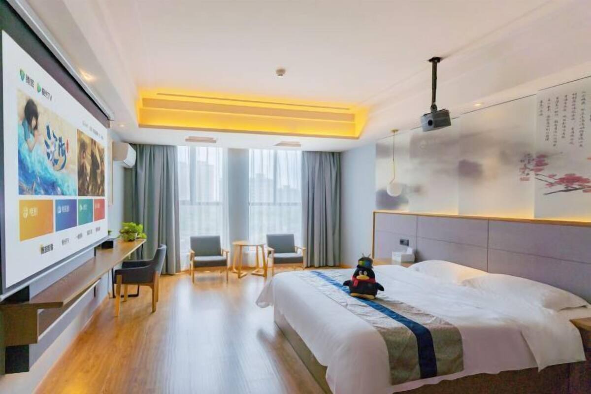 A hotel room with a bed, a desk, two chairs, a TV, and a large window.