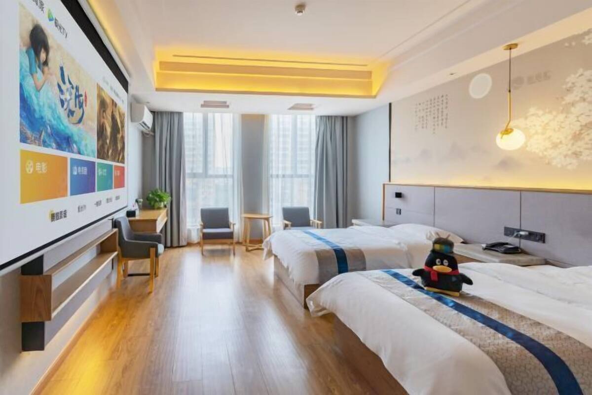 A hotel room with two beds, a desk, a chair, a TV, and a wall with a poster.